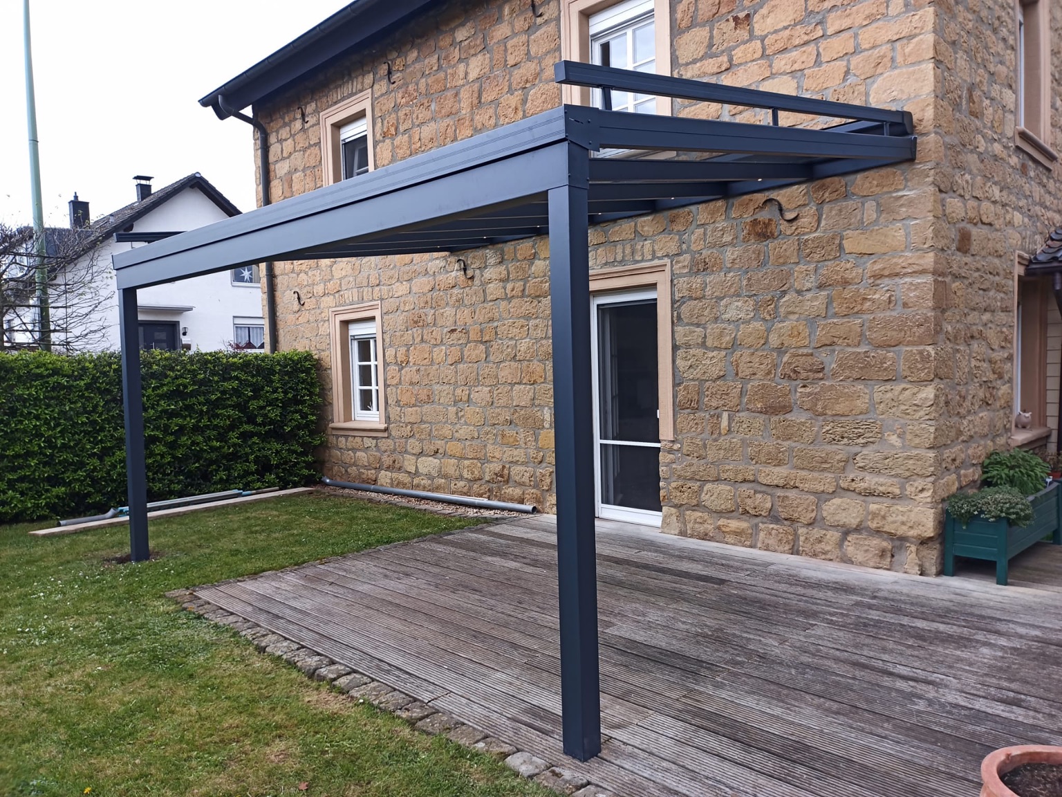 Terrassenüberdachung mit Glasdach ohne Seitenelemente an einer Natursteinfassade